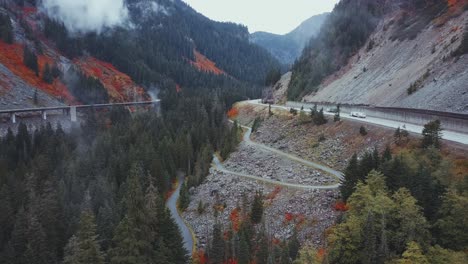 Estado-De-Washington:-Aumento-Aéreo-De-Drones,-Bosque-De-Pinos-Brumosos-Y-Montañas-Con-Una-Carretera,-Camiones-Y-Automóviles,-Y-Colores-Rojos-De-Otoño-Cerca-De-Franklin-Falls-Y-Snowqualmie