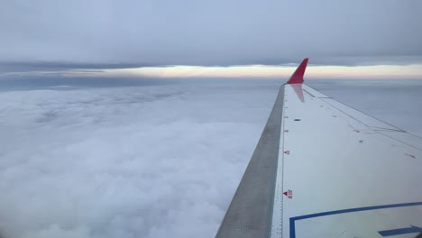 right jet wing with red winglet while flying between layers of clouds