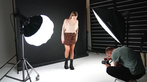 backstage of photographer's work in modern studio. photographer squatted and hold the camera low to take a good shot of modern boots on model girl.