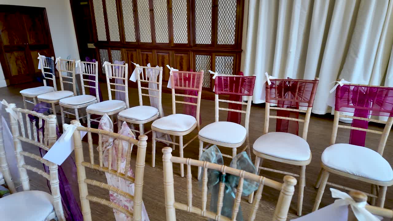 Preparativos en un lugar de celebración de bodas, con filas de sillas decoradas con cintas y cojines blancos, listo para un evento o celebración en un espacio interior con cortinas