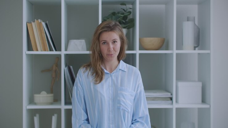 Ung kvinde med krøllet hår taler. Kvinde til jobsamtale. Teenager pige blogger/vlogger laver online videoopkald, optager vlog/blog, taler til kameraet og kigger på webcam indendørs derhjemme.