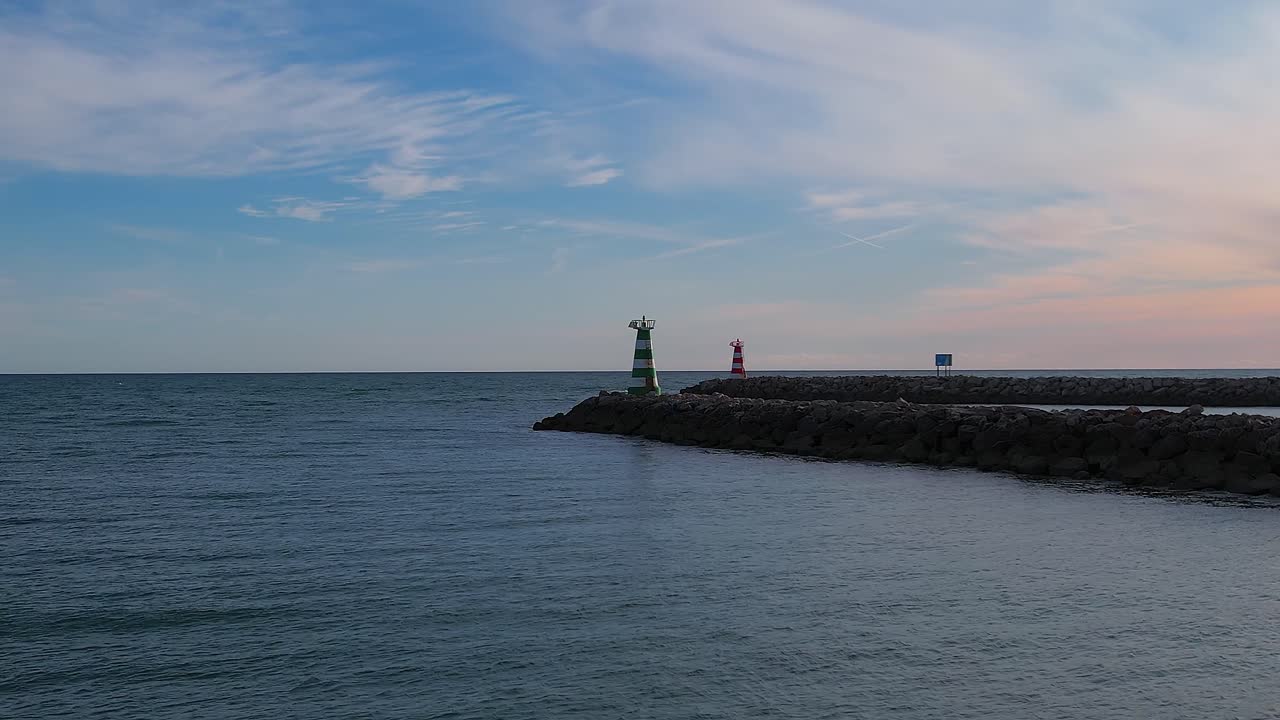 Aerial wide shot capturing the renowned Vilamoura Marina entrance channel with a guiding lighthouse situated at the end of the long jetty on the Algarve coastline