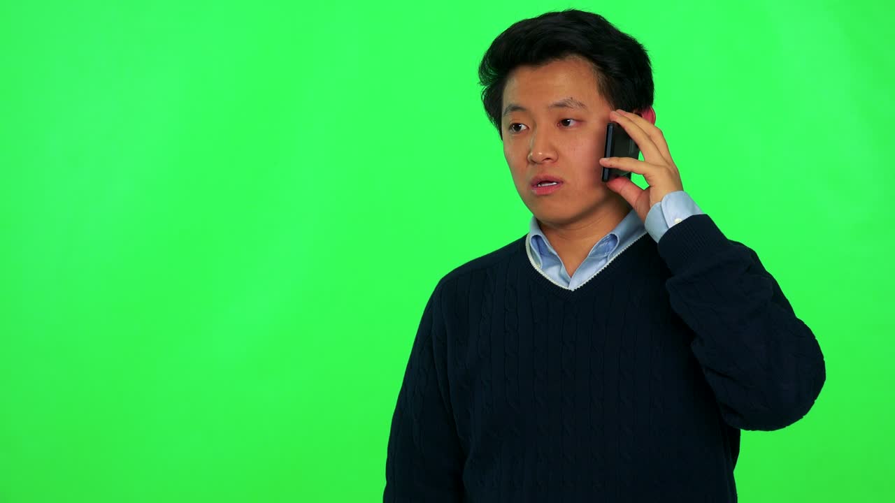 젊은 아시아인 남자가 미소 짓고 스마트폰으로 이야기합니다. - 그린 스크린 스튜디오