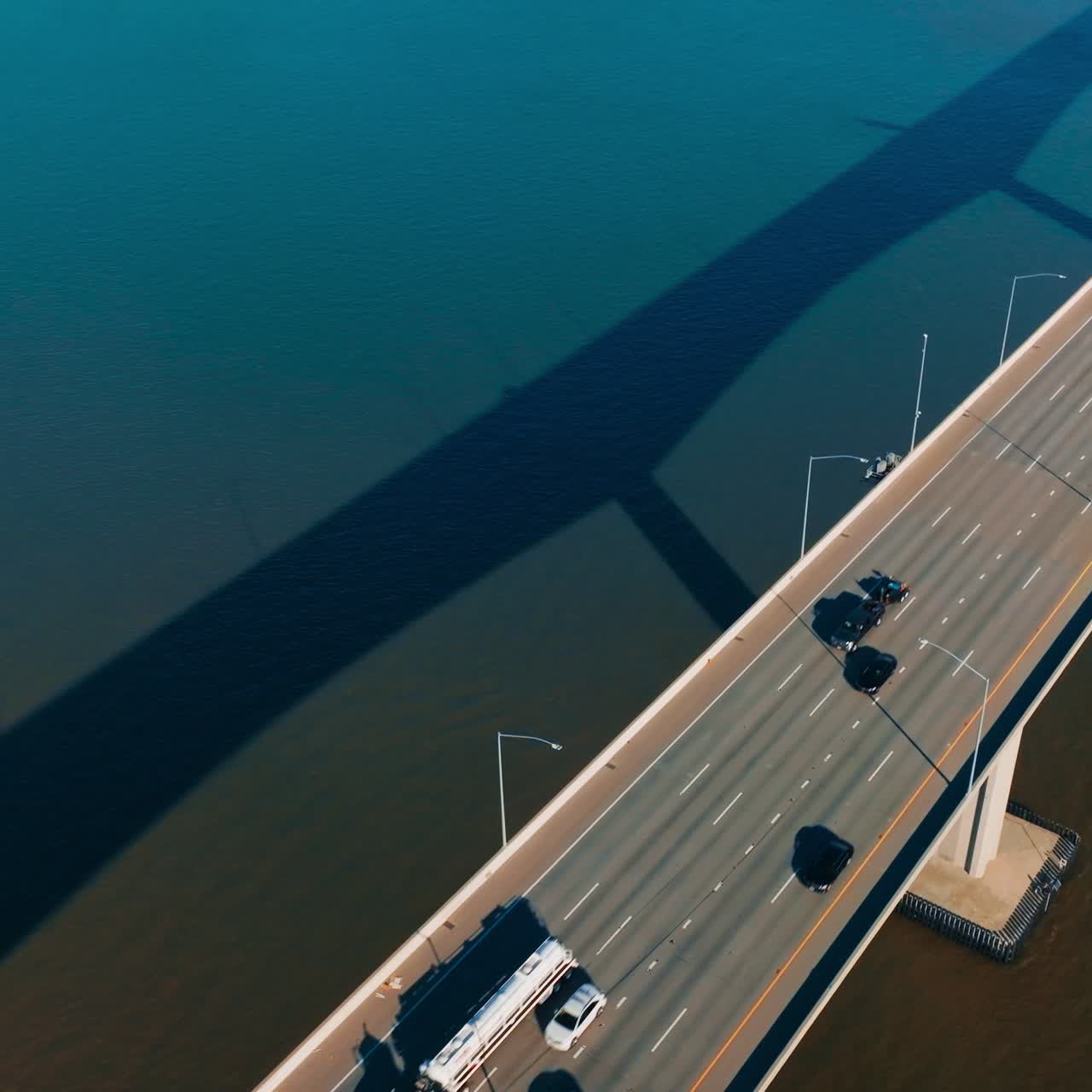Automobile bridge with one-way multi-lane road. Transport moving by the bridge over the calm blue water. Top view