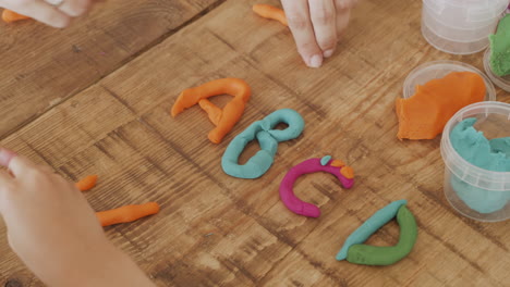 toma de detalle de las manos de una niña jugando con plastilina y creando letras de colores