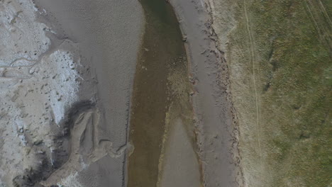 vista aérea de arriba hacia abajo que muestra una trinchera de agua en una bahía costera durante la marea baja