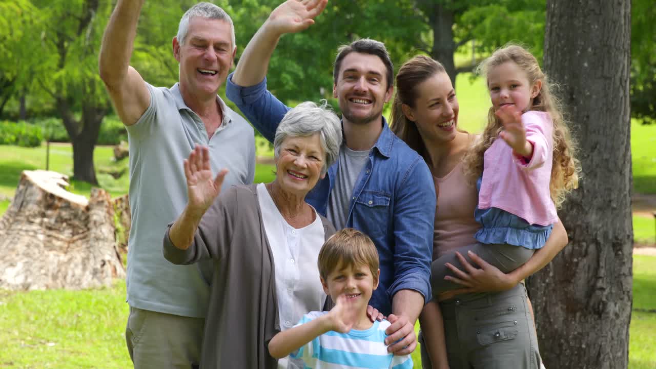 familia de varias generaciones sonriendo y saludando a la cámara en un parque