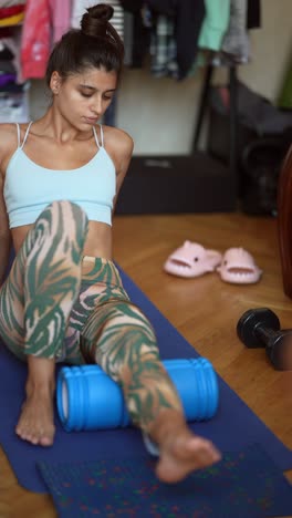 mujer haciendo estiramientos de piernas con rodillo de espuma en casa