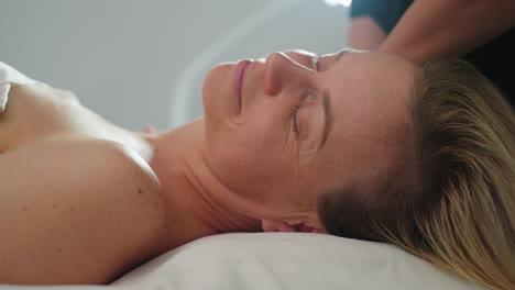 close up of woman closing eyes and breathing deeply expressing relaxation as massage therapist glides fingertips from side of neck to shoulder applying gentle pressure in serene spa environment