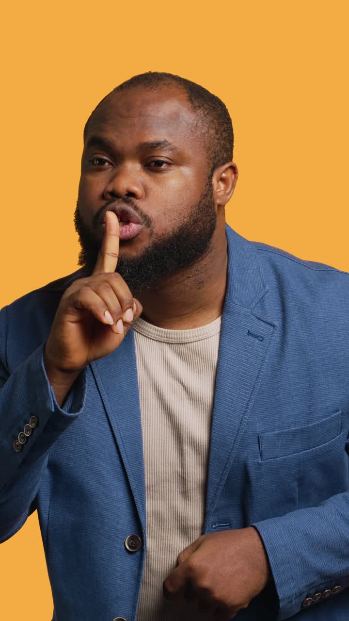 Vertical video Man doing shushing hand gesturing, irritated by noise, studio background