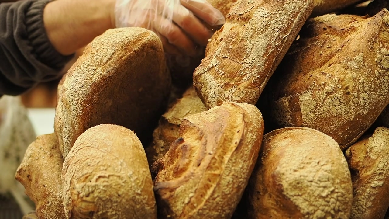 Close-up of Hand Picking a Rustic Bread Loaf from a Pile