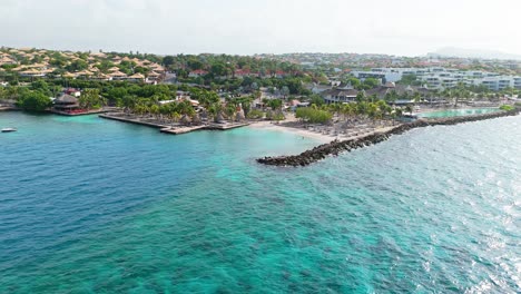 Drone-push-in-to-resort-beach-and-clear-turquoise-Caribbean-waters-by-Jan-Thiel-and-Zanzibar-beach,-Curacao