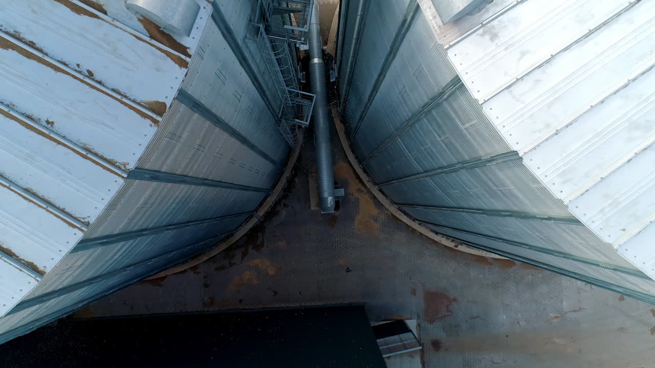 Large metal hangar. Grain elevators outdoors. Aluminum containers for storing grain. Agribusiness. Modern industrial plant. Motion down.