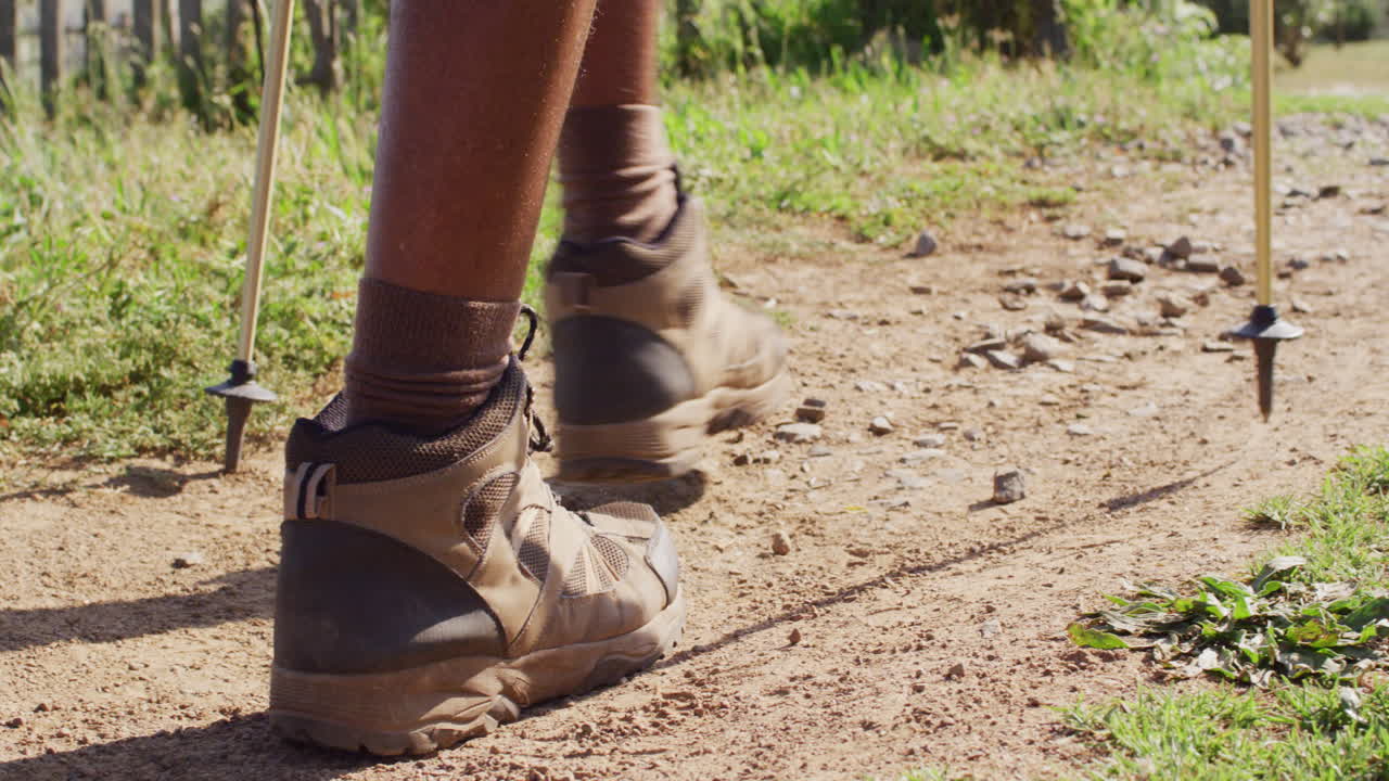 Low section of senior african american man hiking with trekking poles, slow motion
