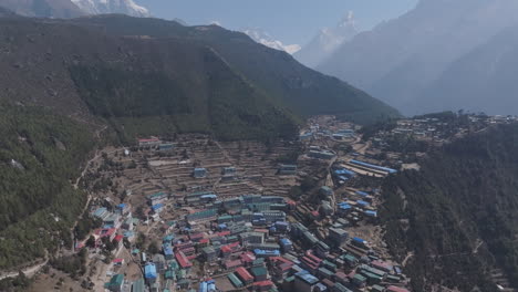 drone shot of village in nepal’s everest region, nestled in hills and forest, with mountains and horizon lit by sunlight creating cinematic landscape