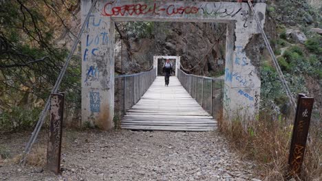 man walks across pedestrian footbridge over rocky river canyon in peru