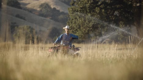 la mano del rancho viaja a través de rociadores de agua en su atv en cámara lenta