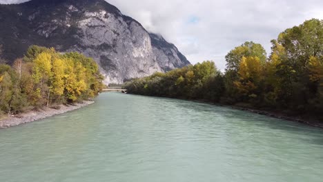 volando a lo largo de un río con árboles creciendo a su alrededor, montañas y puentes en la distancia en un día soleado, innsbruck austria