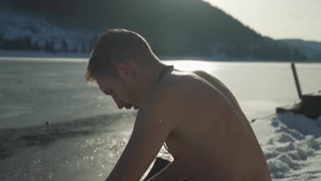 Hombre-Sin-Camisa-Sentado-En-La-Nieve-Junto-Al-Lago-Congelado