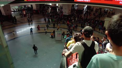 a bustling indoor shopping center with a crowd and a boy looking down from a railing