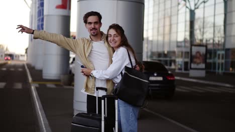 Pareja-Joven-Y-Elegante-Con-Equipaje-Parado-En-El-Estacionamiento-Del-Aeropuerto-Con-Sus-Maletas