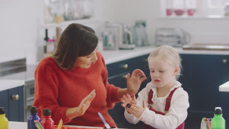hija mostrando a la madre las manos desordenadas mientras pintan una imagen en la cocina