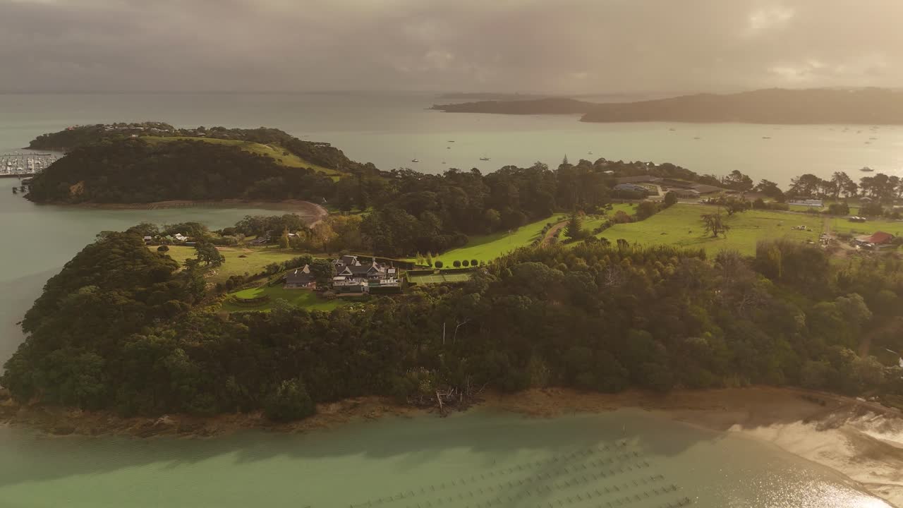 Haiheke Island with tropical plants and Bridge during Sunset time,. Aerial backwards wide shot. Cloudy day in the Evening, New Zealand.