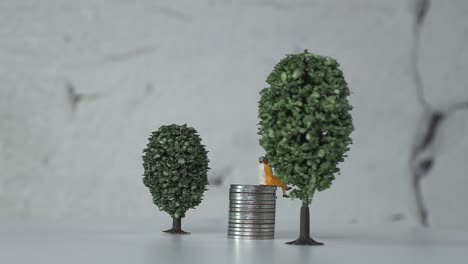 personas en miniatura de la edad en una pila de monedas entre árboles en miniatura.