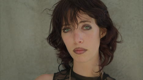 outdoor fashion portrait of young alternative style woman with tattoos and piercing standing against wall shot in real time