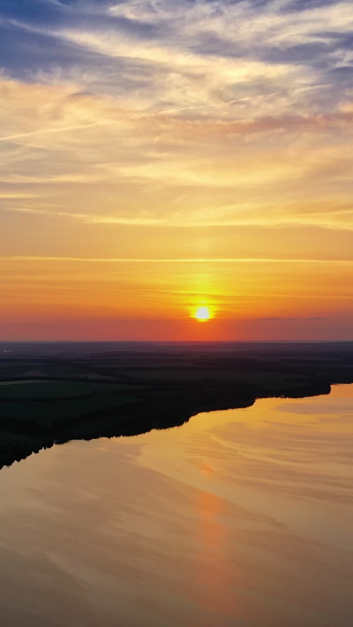 Beautiful river background among fields at dusk. Natural summer landscape in the evening. Calm river at sunset. Aerial view. Vertical video