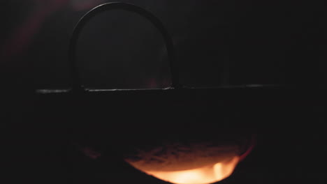another dark, intimate shot of a wok over a flaming woodfire on a clay stove, capturing the raw atmosphere of rural bangladeshi cooking.