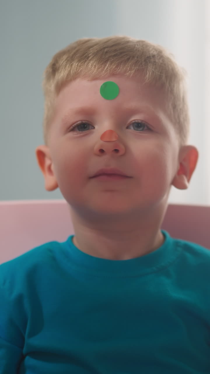 Preschooler girl hand glues dot stickers on little boy nose having fun at home closeup slow motion. Colorful stickers for art development. Decorate face