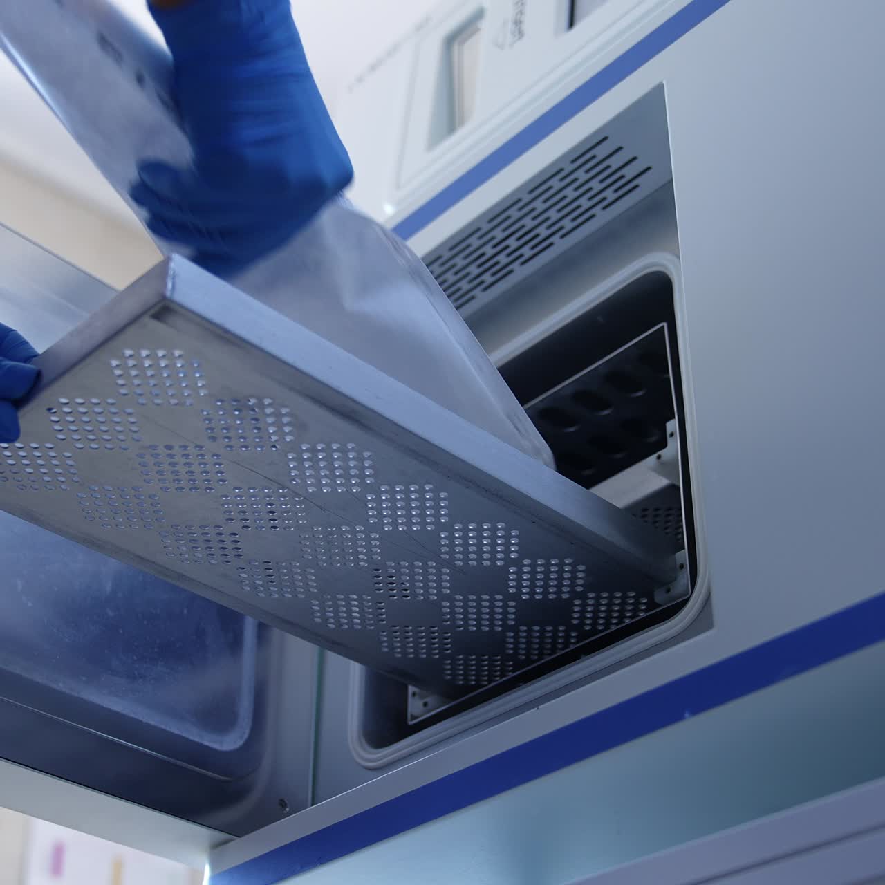 Medic in mask and blue uniform opens the door of machine and puts the tool in plastic bag inside. Sterilization equipment from low angle view