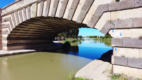 Canal-Du-Midi-Beautiful-bridge-outside-Le-Somail-with-boat-moored-on-the-canal-on-a-very-warm-September-day