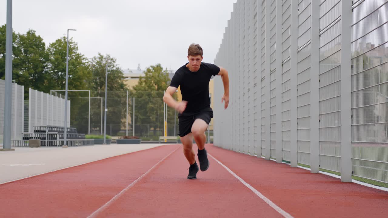 Frontal view of young white male athlete placing hands down preparing to sprint on track