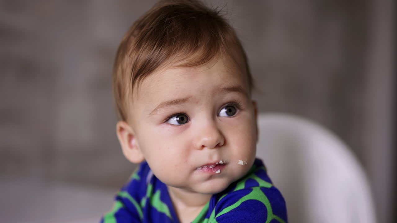 Beautiful Caucasian child eating porridge. Woman's hand giving a full spoon to a boy but he turns away. Close up.