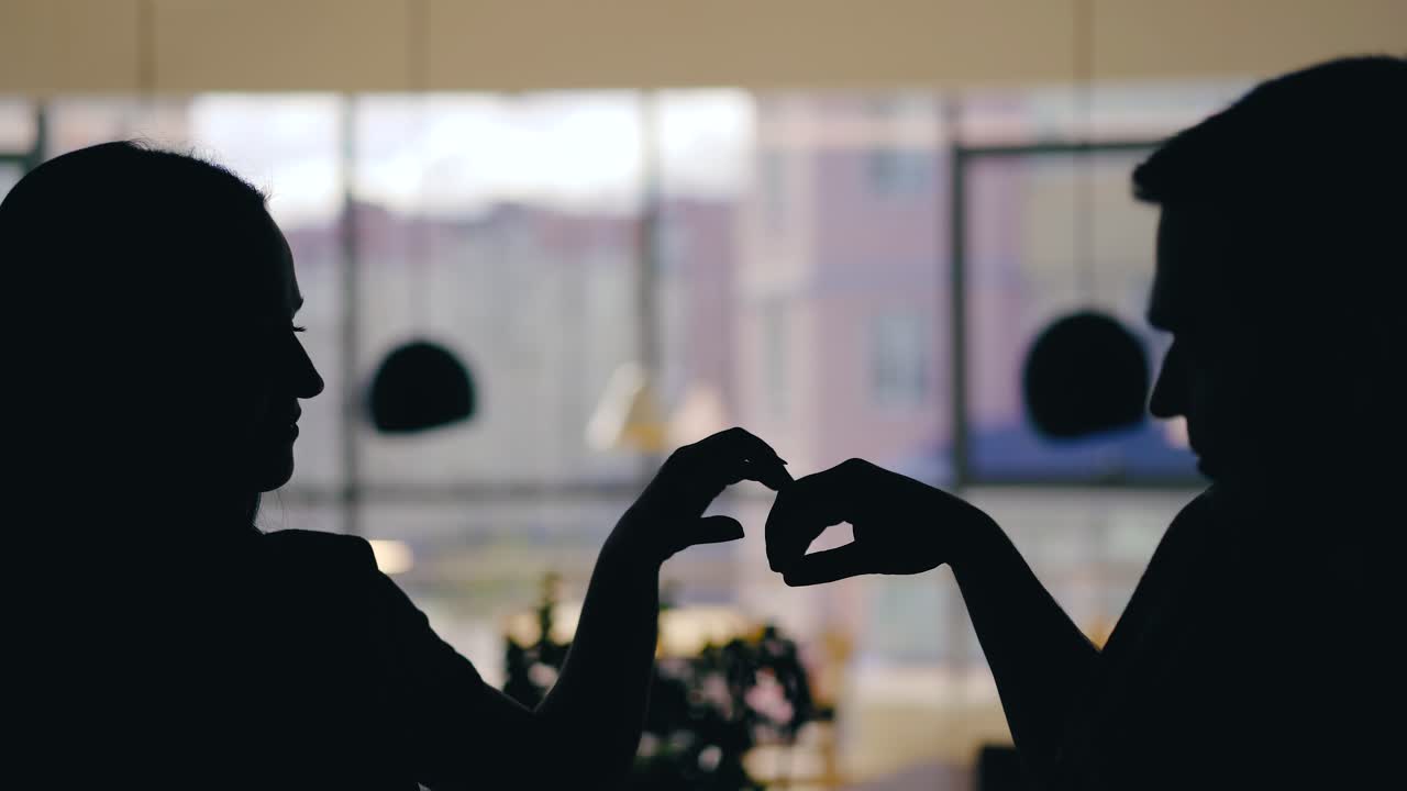 silhouettes of man and woman are talking at a table in the cafe and drinking drinks on the background of the window. Blurred background