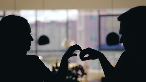 silhouettes of man and woman are talking at a table in the cafe and drinking drinks on the background of the window. blurred background