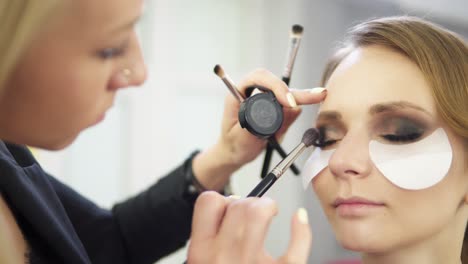 artista de maquillaje aplicando sombra de ojos en el párpado usando pincel de maquillaje y protegiendo la piel con parches blancos. maquillaje profesional. filmado en 4k