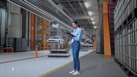mujer inspeccionando coches en una línea de ensamblaje en una fábrica moderna.