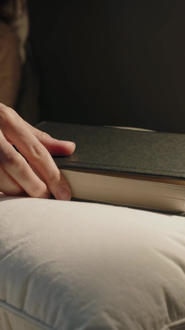 Video verticale: Donna in maglione che posa un libro nero con segnalibro rosso sul cuscino del letto dopo aver letto.