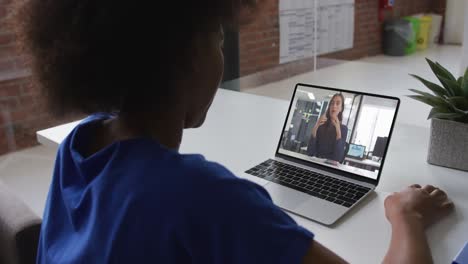 Mujer-De-Negocios-Afroamericana-Sentada-En-El-Escritorio-Usando-Una-Computadora-Portátil-Teniendo-Una-Videollamada-Con-Una-Colega