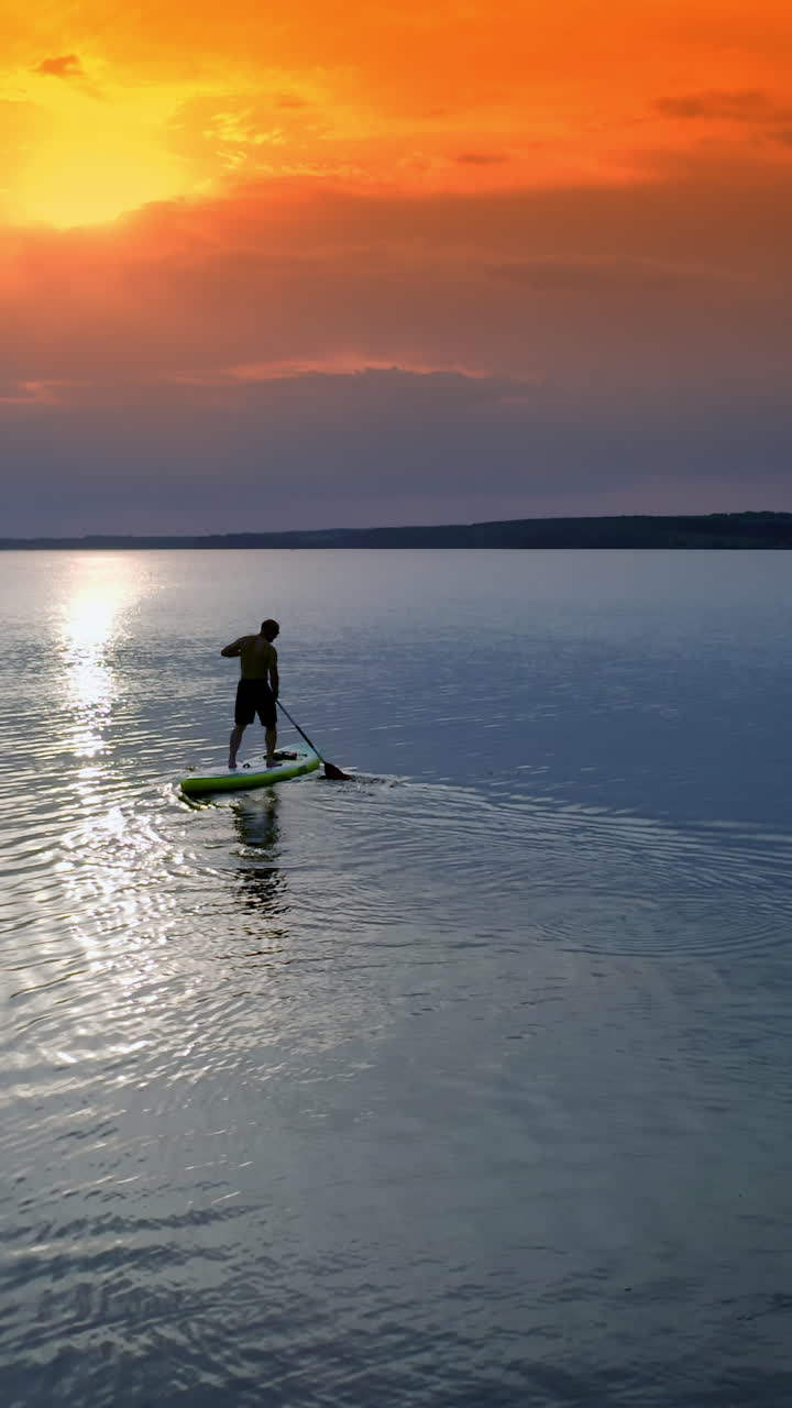 Man sailing on river. Sports training on water against beautiful sunset. Athlete is rowing on the evening water while standing with an oar. Water sports. Vertical video