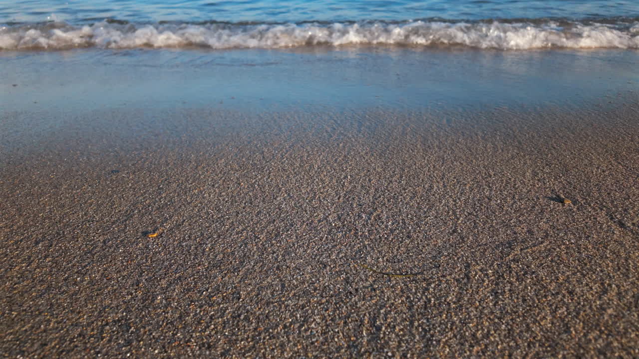 Close up of gentle sea waves washing over wet sand at the shoreline