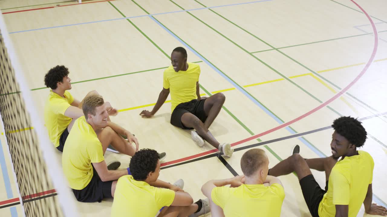 Ein diverses männliches Team in gelben Trikots erreicht sitzende Spieler, passt den Volleyball und ruht sich auf dem Spielfeld aus.