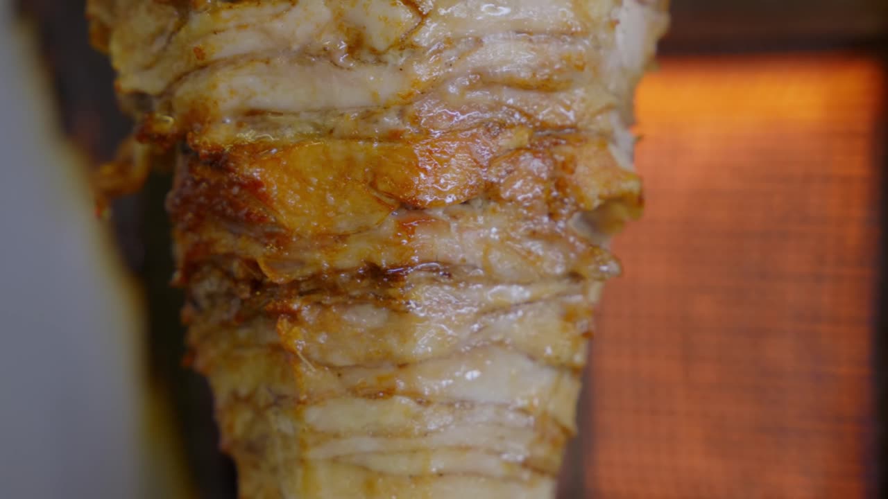 Spiedo di shawarma di pollo appeso sulla griglia che gira vicino a un forno a gas