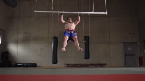 joven boxeador haciendo burpees y pull ups en un gimnasio de boxeo vacío como entrenamiento