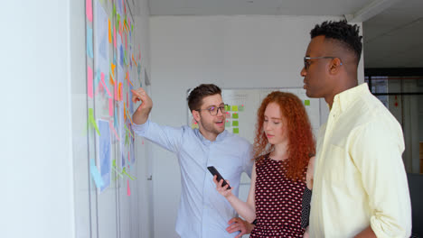 Side-view-of-young-mixed-race-business-team-planning-and-working-on-glass-wall-in-modern-office-4k