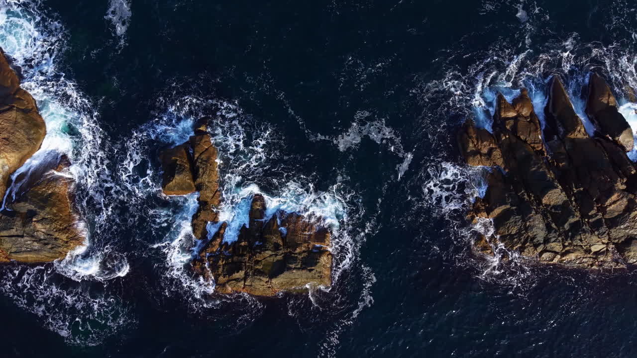 Waves crashing on rugged coastal rocks under a clear sky at dusk, creating a dramatic and serene ocean landscape