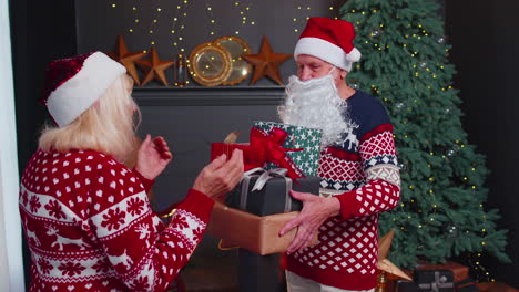 Grandfather-Santa-Claus-gifting-Christmas-present-box-to-surprised-grandmother,-senior-couple-family